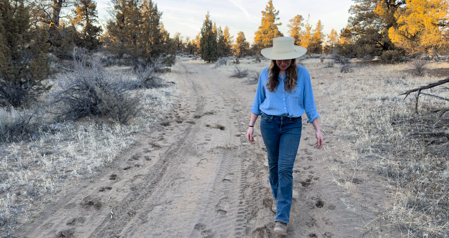 Rebecca walking down a dusty road surrounded by juniper trees